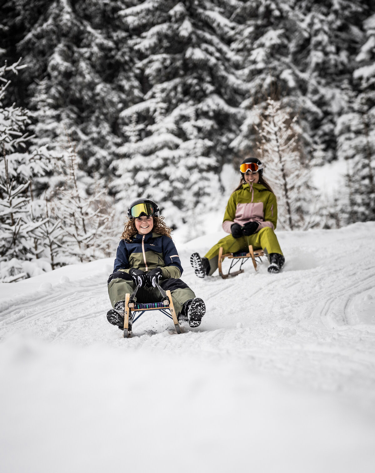 Mutter und Tochter beim gemeinsamen Rodeln auf der Gnadenalm in einer verschneiten Winterlandschaft.