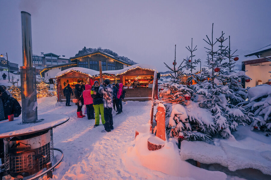 Verschneiter Tauernadvent mit festlich beleuchteten Holzhütten, geschmückten Tannenbäumen und Besucherinnen und Besuchern in winterlicher Abendstimmung.