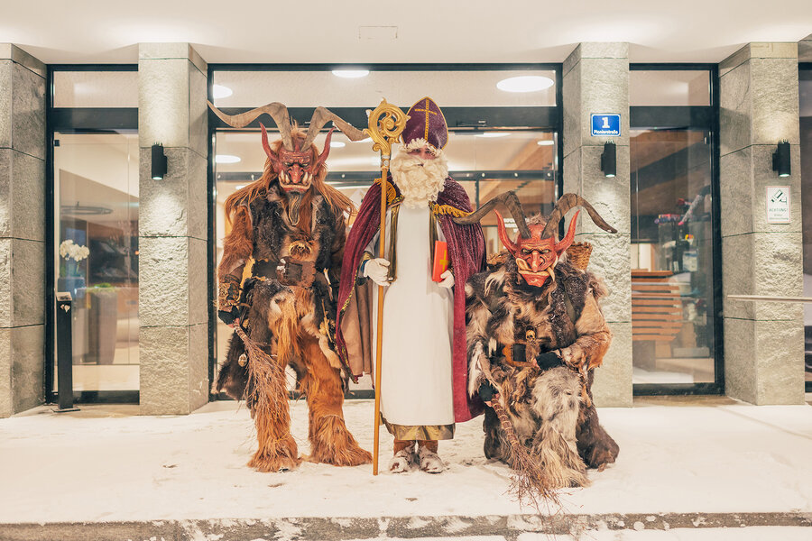 Nikolaus und zwei traditionell kostümierte Krampusse begrüßen Besucher vor einem verschneiten Gebäude beim Tauernadvent.