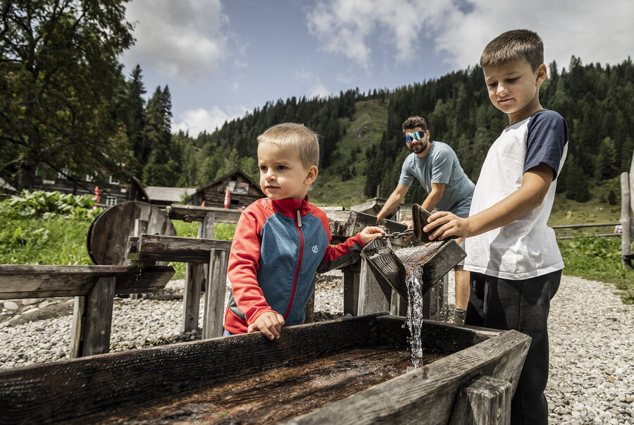 Kinder spielen am Wasserspielplatz mit Holzrinnen in alpiner Umgebung