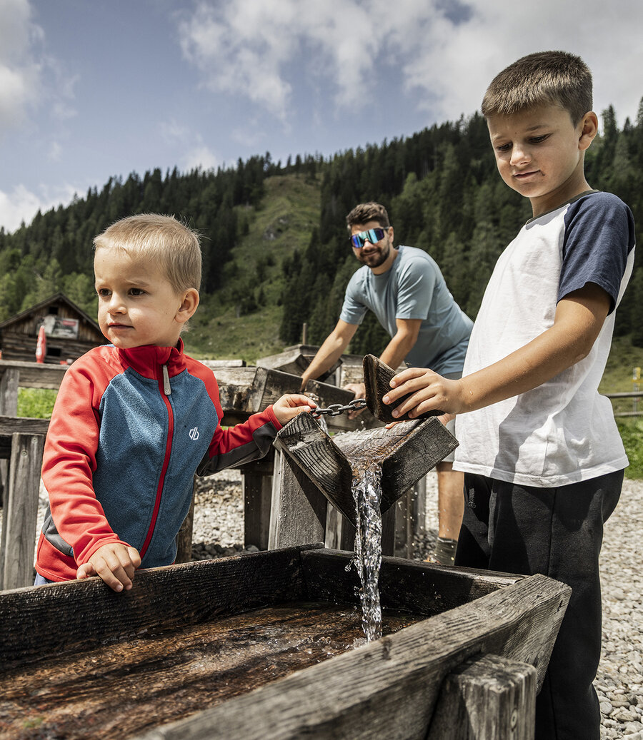 Kinder spielen am Wasserspielplatz mit Holzrinnen in alpiner Umgebung